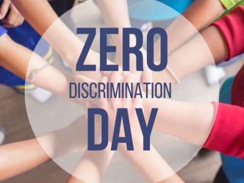 The image depicts a group of individuals, their identities not visible, joining hands in a circle from an overhead perspective. The central graphic, with the text "ZERO DISCRIMINATION DAY," suggests a message of unity and the commitment to fight against discrimination in all its forms.