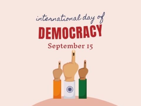 Graphic for International Day of Democracy showing three raised hands painted with the colors of the Indian flag, with the middle finger marked with a voting ink indicating participation in democracy. Text above reads 'International Day of Democracy September 15'.