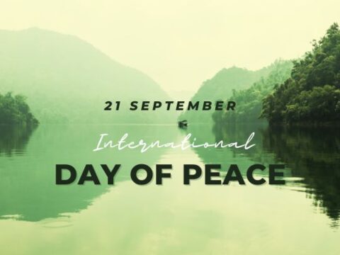 The image depicts a serene landscape of a tranquil lake surrounded by mountains, overlaid with text celebrating the "21 September - International Day of Peace." This calming natural scene effectively symbolizes the concept of peace.