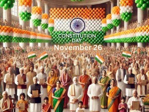 The image showcases a large gathering of diverse Indian people in a grand hall, celebrating Constitution Day on November 26. The setting is decorated with orange, white, and green balloons, reflecting the colors of the Indian flag. In the center, prominent figures in traditional and formal attire hold the Indian Constitution. The crowd, consisting of people of various ages and backgrounds, appears united and proud, symbolizing national unity and respect for the country's constitutional values.